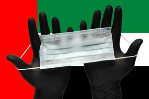 Doctor holding medical mask for face in two hands black gloves on background national flag of United Arab Emirates UAE. Concept quarantine, pandemic insurance coronavirus photo