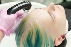 Professional hair salon, hairstylist washing customer head with green hair color photo