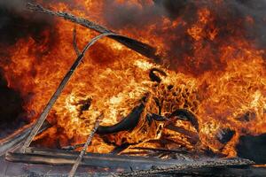 Burning cars wheels, flame of red-orange fire, clouds of black smoke in sky photo