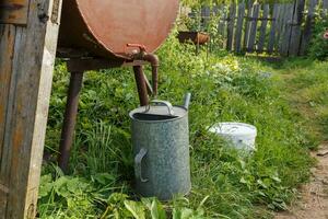 Rain barrel and watering can in vegetable garden photo