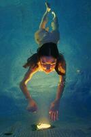 Female swims in geothermal pool, reaches out hands to illuminated lights from pool lamp at night photo