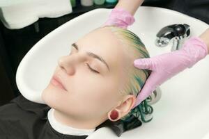 Hairdresser lathers clients head with hair conditioner, washing head in special sink in beauty salon photo
