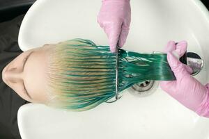 Top view of hairdresser in protective glove holds hair in hand and combs long green and discolored hair of customer while washing hair in shower photo