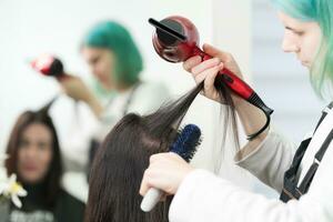 estilista se seca morena pelo con rojo pelo secadora, azul cepillo para el pelo en belleza salón foto