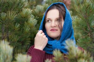 Portrait of sweet brunette woman with brown eyes and long hair stands in fir forest, looking to side photo