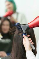 manos de estilista se seca morena pelo de cliente utilizando pelo secadora y peine en belleza salón foto