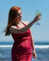 Redhead woman in red dress holding glass of white wine at eye level and looking at him photo