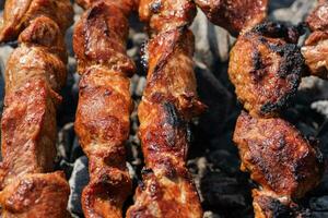 Pork shish kebab cooking on skewers on charcoal grill with fire smoke photo