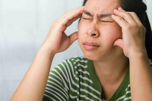 Young woman having headache against white curtain background in room. An adult woman touching head because of headache or migraine. Hands on head. photo