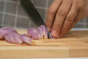 hembra mano utilizando cuchillo a rebanada Fresco rojo cebolla en el cortar junta, de cerca. cocinero el cortar chalotes utilizando un agudo cuchillo en un de madera el cortar tablero. preparando hecho en casa comida foto