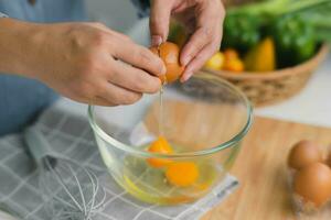 Young woman cooking in a bright kitchen, hand made cracked fresh egg yolks dripping into the bowl. Preparing ingredients for healthy cooking. Homemade food photo