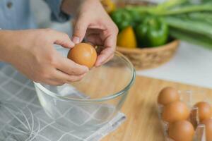 Young woman cooking in a bright kitchen, hand made cracked fresh egg yolks dripping into the bowl. Preparing ingredients for healthy cooking. Homemade food photo