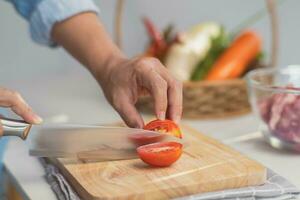 Cocinando - del chef manos son corte Tomates en el el cortar tablero en el cocina. preparando Cerdo valores con vegetales caldo en un maceta. hecho en casa caldo receta. foto