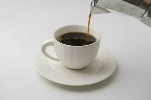 Hand holding Mokapot pouring coffee into white cup on table. Black coffee in white cup isolated on white background photo