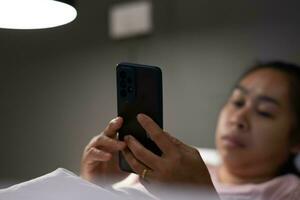 Young Asian woman lying on white bed and playing smartphone at night. Woman in bed with phone. Health and social concept. photo