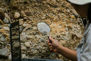 de cerca de hembra geólogo utilizando aumentador vaso a examinar y analizar roca, suelo, arena en naturaleza. arqueólogos explorar el campo. ambiental y ecología investigación. foto