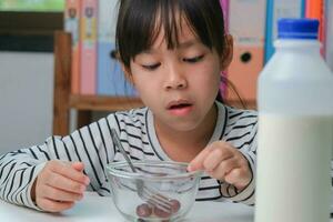 Little girl eating fresh red grapes at home in the living room. Cute young Asian girl eats healthy fruits and milk for her meal. Healthy food in childhood photo