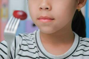 Little girl eating fresh red grapes at home in the living room. Cute young Asian girl eats healthy fruits and milk for her meal. Healthy food in childhood photo