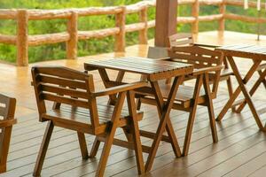 Wooden tables and chairs at outdoor cafe terrace in park. Empty garden furniture surrounded by green garden. photo