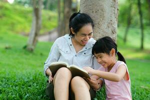 Happy mother and little girl having fun and enjoying reading at the park. Mother and daughter resting in the summer garden, she reads fairy tales to her daughter. photo