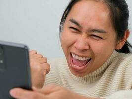 Portrait of happy woman enjoying success on mobile phone at home. Close-up of happy young woman reading good news on the phone. Surprised woman celebrating success on the phone. photo