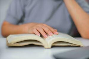 Closeup image of Asian woman sitting at a table reading a book in the living room. photo