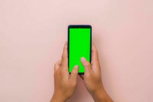 Human hand using mobile smartphone with mockup green screen on pink background. Male hand tapping and pinch to zoom in or zoom out on blank digital screen. photo