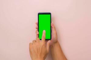 Human hand using mobile smartphone with mockup green screen on pink background. Male hand tapping and pinch to zoom in or zoom out on blank digital screen. photo