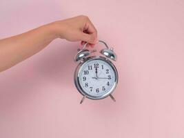 Female hand holding classic alarm clock on pink background. Close up of alarm clock in hand. photo