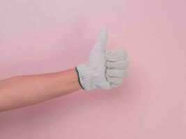 Hands in white knitted gloves isolated on pink background. Female hand showing thumb up with cotton gloves. photo