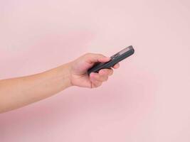 Hand pressing remote control isolated on pink background. Remote control in human hand. photo