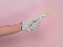 Hand in white knitted glove holding paint brush isolated on pink background. photo