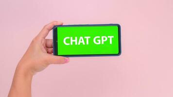 Human hand holding mobile smartphone with Chat GPT green screen in horizontal position isolated on pink background. Chat bot assistant or artificial intelligence Ai Chat GPT. photo