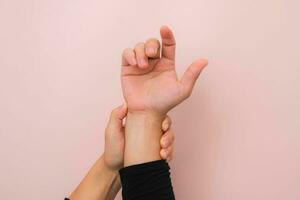 Close-up of woman's hand holding her painful wrist from Arthritis or Carpal Tunnel Syndrome  isolated on pink background. Health care concept. photo