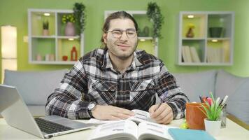 contento masculino estudiante estudiando a escritorio y mirando a cámara sonriente. video