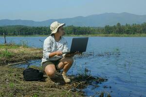 Female environmentalist using laptop computer to record pathogen analysis in natural water. Water and ecology concept photo