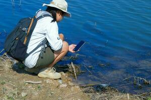 hembra ambientalista utilizando móvil teléfono a grabar análisis de patógenos en natural aguas agua y ecología concepto foto