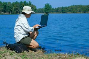 Female environmentalist using laptop computer to record pathogen analysis in natural water. Water and ecology concept photo