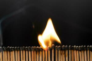 Rows of matches burning with flames close-up. View of the matches as they burn and smoke. Shot of igniting matches against black Background. photo