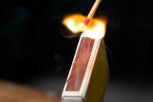 Matchstick fires on matchbox in slow motion close-up. The match was being lit, a blazing fire. Shot of igniting match against black Background. photo