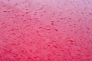 Water droplets from rain on a red metal hood of a car. Rain drops on red car hood. Selective focus photo