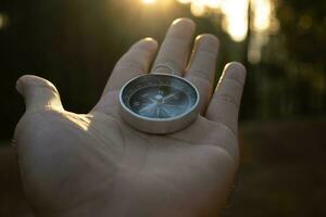 Compass in hand on natural pine forest background. hand holding compass in forest landscape. Young traveler searching direction with compass in summer mountains. photo