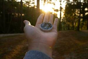 Compass in hand on natural pine forest background. hand holding compass in forest landscape. Young traveler searching direction with compass in summer mountains. photo