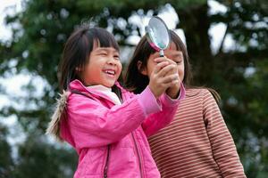 Two happy sisters exploring nature with magnifying glass outdoors. Child playing in the forest with magnifying glass. Education and discovery concept. photo