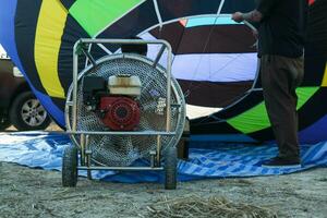 Looking Inside hot air balloon while on the ground and preparing for a flight. A balloon pilot inflates a hot air balloon with a large fan while a wicker basket lays sideways on the ground. photo