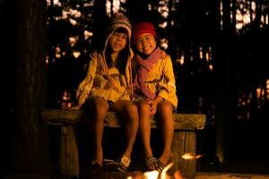 lindas hermanitas se calientan cerca de la fogata al aire libre cuando hace frío. niños divirtiéndose en el fuego del campamento. acampar con niños en el bosque de pinos de invierno. familia feliz de vacaciones en la naturaleza. foto