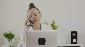 une femme séance à une bureau avec une portable et parlant sur le téléphone video