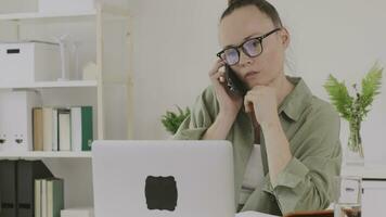 a woman sitting at a desk with a laptop and talking on the phone video