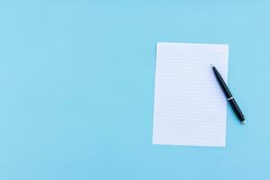 Blank white paper and pen isolated on blue background. After some edits. photo