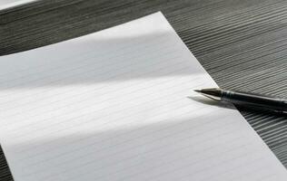 Broken pencil and a blank paper on a wooden textured table with partial shadows, after some edits. photo